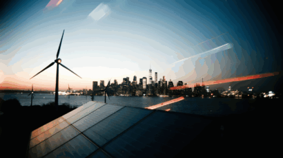 Clean energy wind turbines and solar panels with New York City skyline at sunset