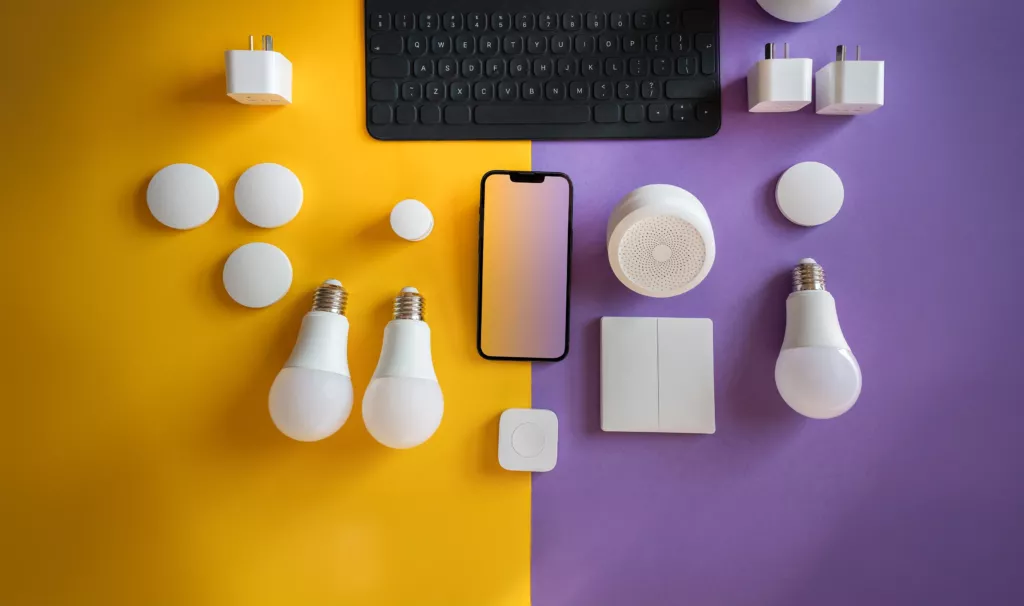 Smart home devices flat lay LED bulbs, smart plugs, switches, and hub on yellow and purple background